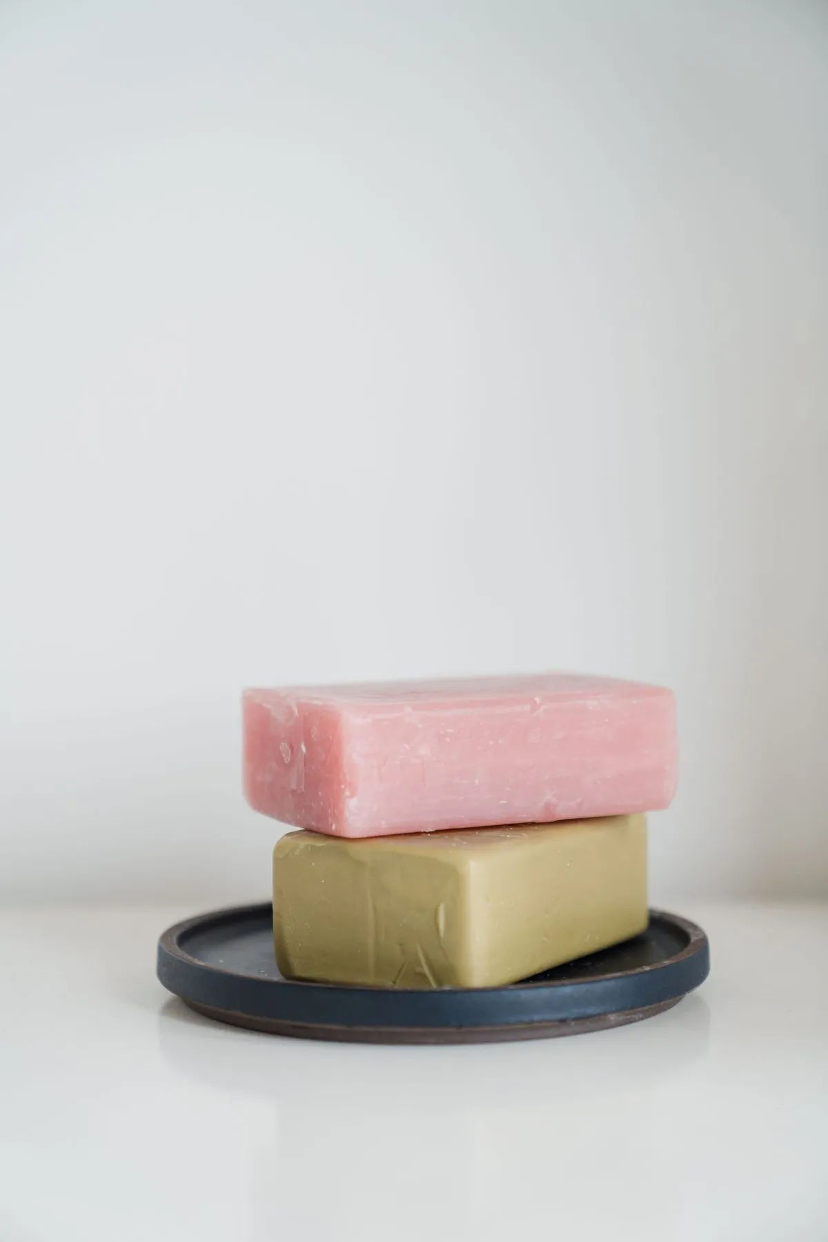 A pink bar and an olive bar of soap, stacked on a slate dish.